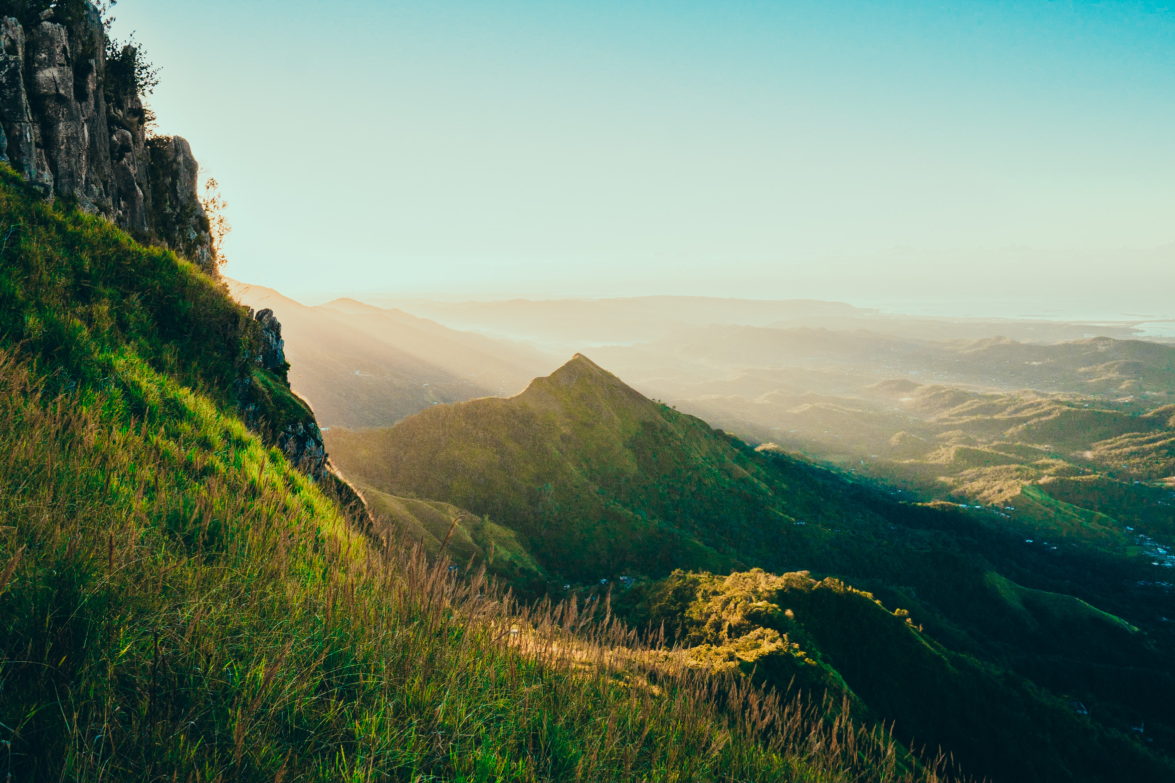A sunlit mountain ridge and green valley viewed from a high cliff